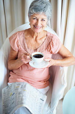 Smiling senior woman drinking coffee while reading newspaper