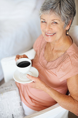 Senior woman drinking coffee while reading newspaper
