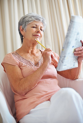 Thoughtful senior woman solving a crossword puzzle in newspaper