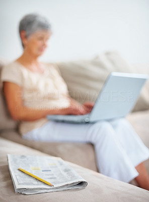 Elderly woman using laptop with newspaper lying in foreground