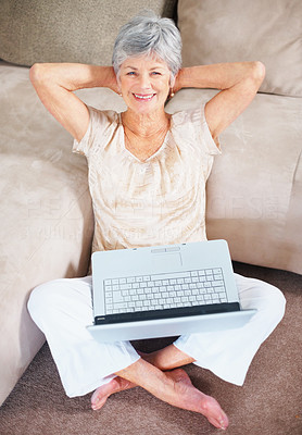 Happy old woman with laptop relaxing by a couch