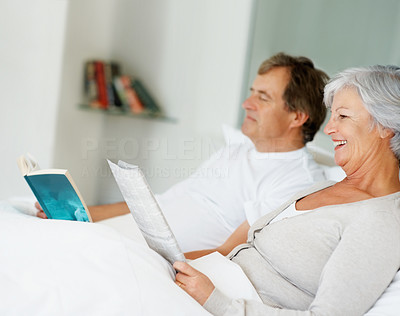 Relaxed happy old couple reading magazine while lying on bed