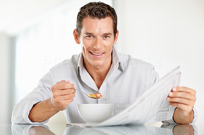 Happy middle aged man with newspaper while having his breakfast