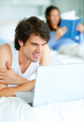 Couple relaxing on bed - Man using laptop and woman reading book