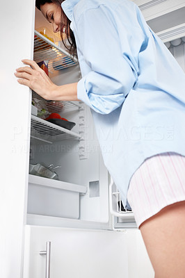 Smiling woman peering into an open fridge at home