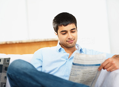 Young man sitting on couch at home reading newspaper indoors