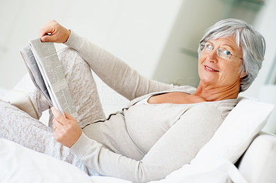 Happy relaxed senior woman with the daily newspaper in bed