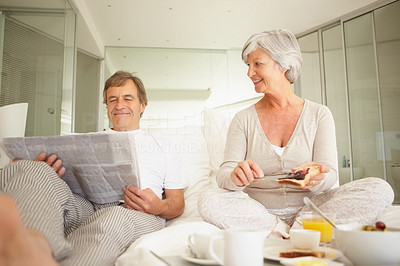 Man reading newspaper while woman preparing breakfast