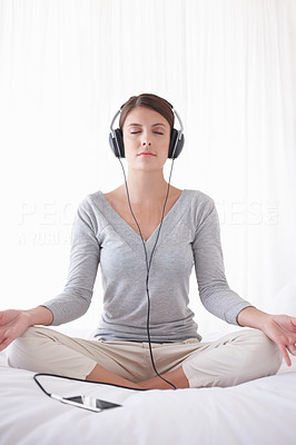 Pretty girl with headphones sitting in lotus position on bed