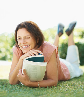 Happy mature woman with a book lying on grass at the lawn