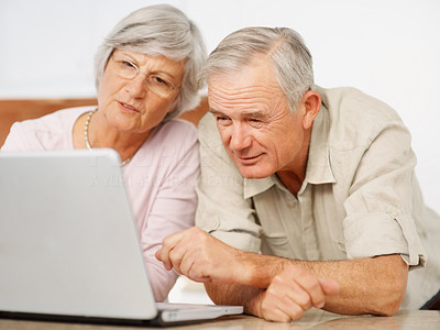 An elderly man and woman browsing the internet on a laptop