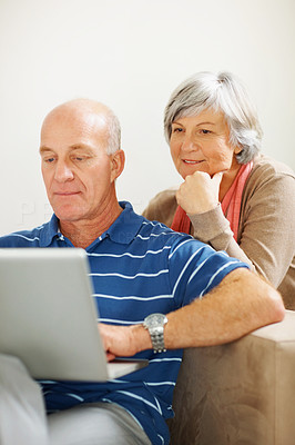 Senior woman watching her husband work on a computer laptop