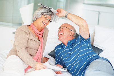 Cheerful senior couple with newspapers having fun on bed