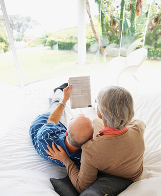 Relaxed senior man and woman reading newspaper on bed