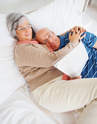 A loving senior man and woman reading newspaper on bed