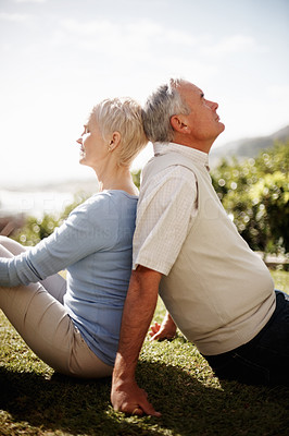 Side view of an elderly couple sitting back to back outdoors