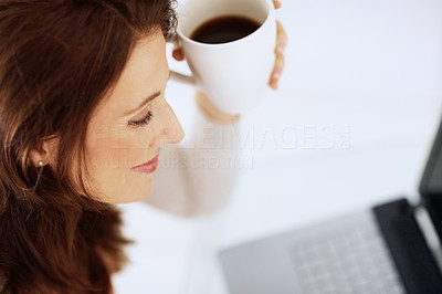 Closeup of a mature woman holding a coffee cup using a laptop