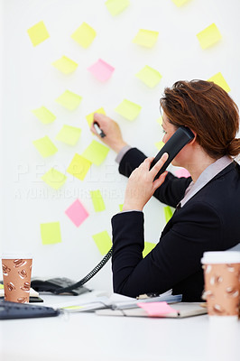 Business woman writing on notes while speaking on phone