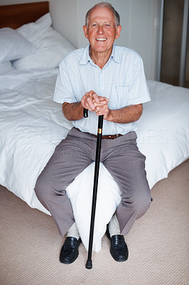 Senior man sitting on a bed , smiling with a walking stick