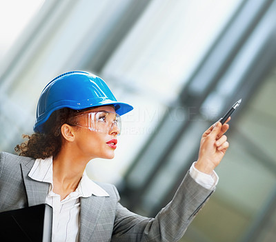 Female architect wearing a hardhat pointing upwards with a pen
