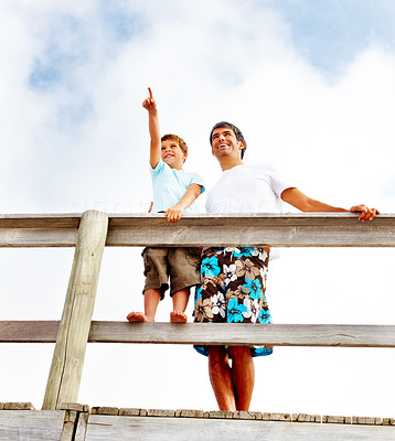 Happy father and son standing on a wooden railing outdoors, son pointing out