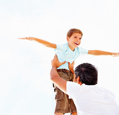 Happy cute boy being lifted up by his father, against the bright sky