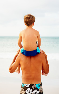Rear view of a father carrying his son on the shoulders while on the beach