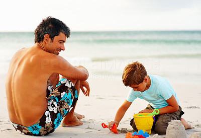 Man watching his son making a sand castle at the beach