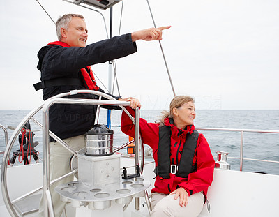 Romantic mature couple on a sea voyage steering the boat, pointing away