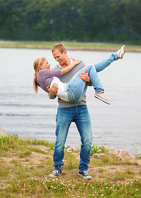 Young guy carrying his girlfriend in his arms, outdoor by the lake