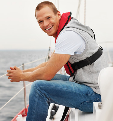 Young man wearing a life jacket sitting in a sailboat at sea