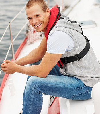 Happy young guy wearing a life jacket sitting in a sailboat at sea