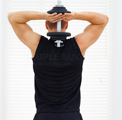 Rear view of a young guy exercising his triceps with a dumbbell
