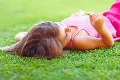 A little girl lying on grass with flower in her hand