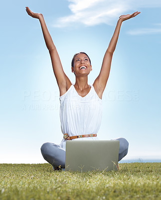 Young woman with raised hands and a laptop on grass