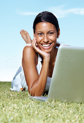 Smiling young lady lying on the grass with a laptop