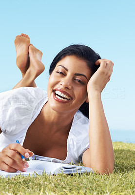 Cheerful woman lying on grass and writing notes