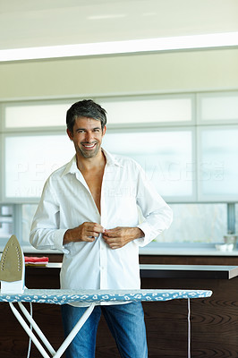 Happy mature man buttoning his white shirt after ironing