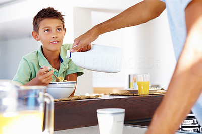 Young boy having a bowl of cereals, father pouring milk for him