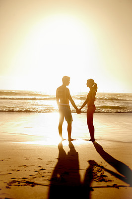 Silhouetted couple holding hands on the beach