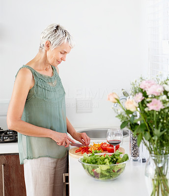 Happy mature woman preparing salad in the kitchen