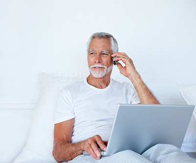 A senior old man speaking on a mobile while working on laptop