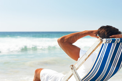 Young man resting by the beach on a deck chair and looking at the ocean