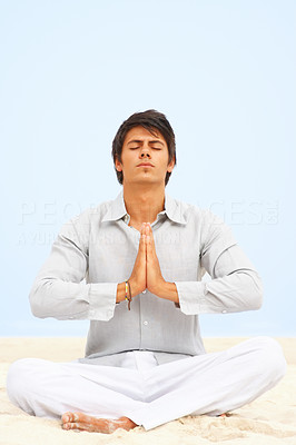 Handsome young man meditating on the beach with his hands joined