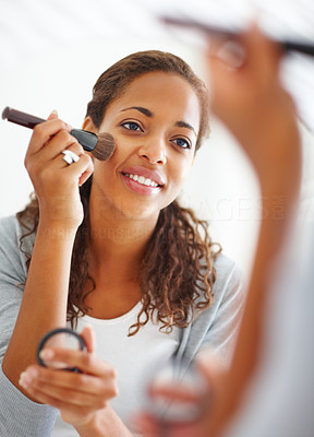 Young woman looking at the mirror and applying blush using a brush