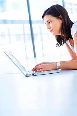 Cute young business woman lying on the floor at home and working on a laptop