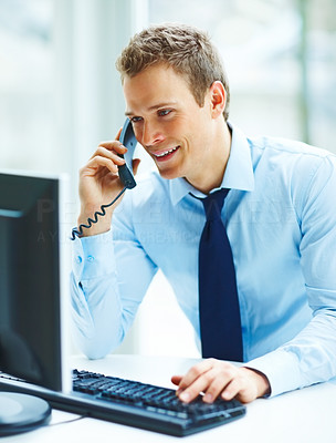 Young busineass man speaking on the phone while working on a computer