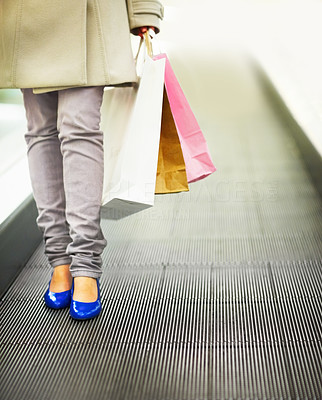 Lower section image of a female coming down a escalator holding shopping bags