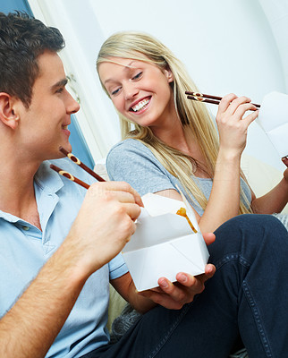 Happy young couple eating from a takeaway container with chopsticks