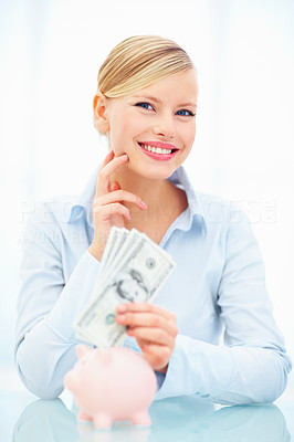 Happy woman holding cash with piggybank on table